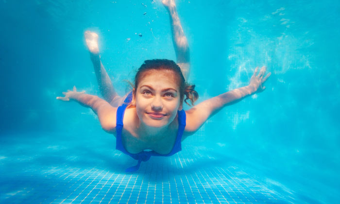 happy teen girl swimming underwater at bottom of pool